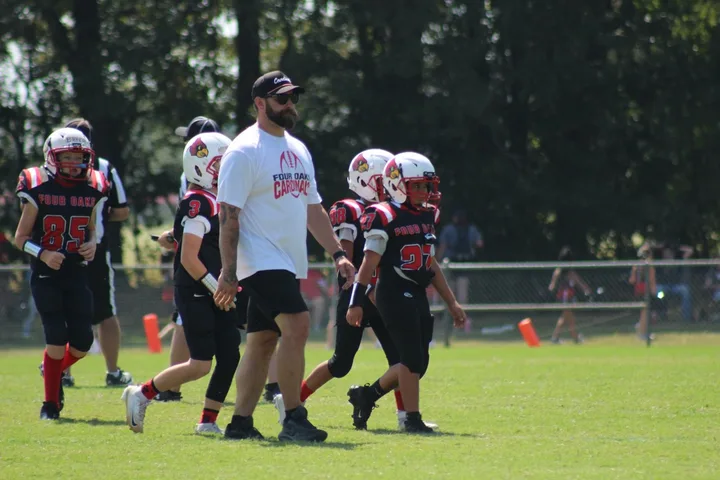 A Four Oaks coach leading Four Oaks players across the field